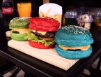 Três hambúrgueres coloridos (vermelho, azul e verde) sobre mesa de hamburgueria.